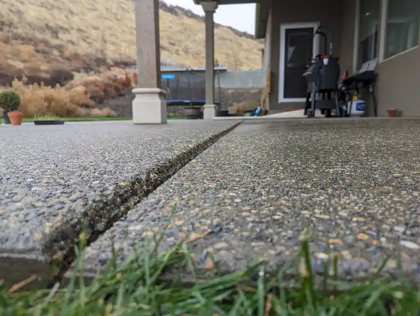 Exposed-aggregate patio joint brought back flush, porch columns and dry hills behind, Toppenish