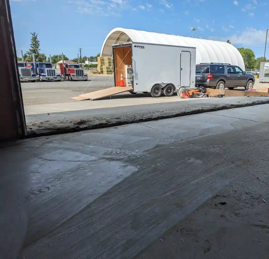 A commercial concrete slab at a roll-up door, with a truck yard and trailer outside