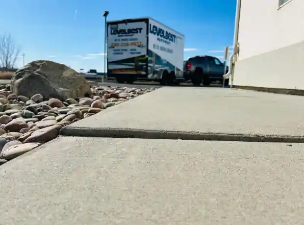 Before: two concrete slabs by a building with a step down at the joint, river rock to one side and our trailer in the distance