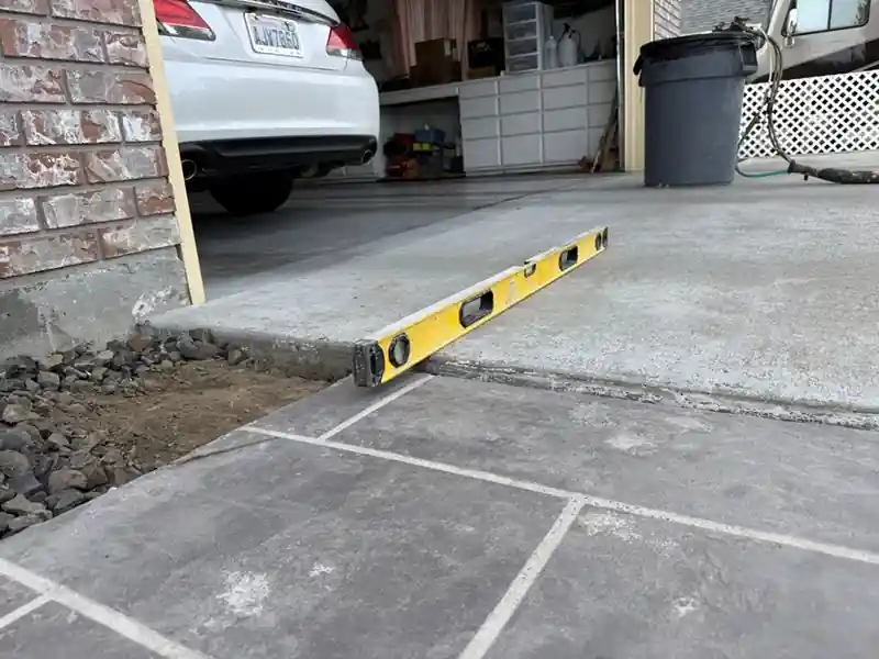 Before: a garage apron sunk below the scored patio beside it, a yellow level rocking on the step