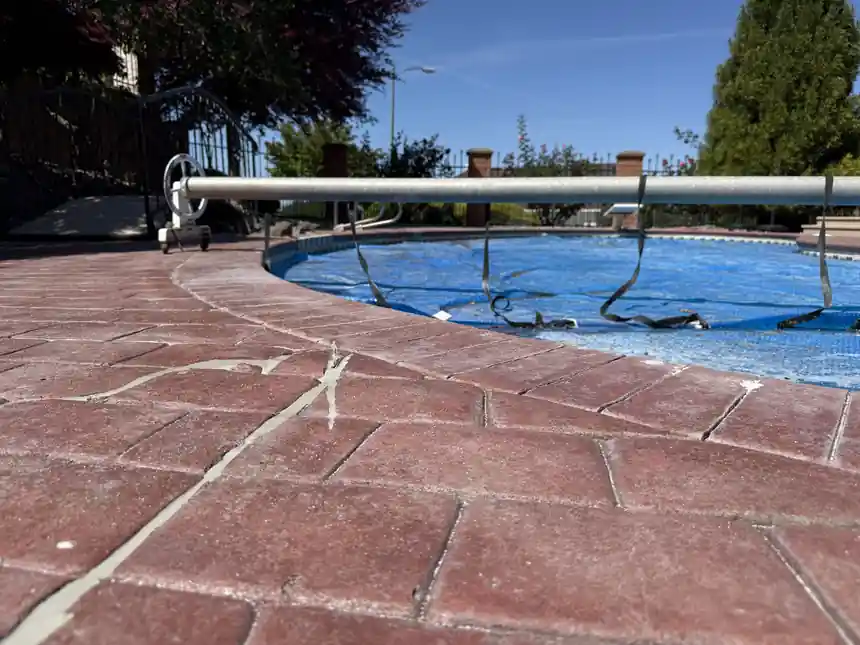 A red stamped pool deck with a crack running through it, pool cover beside it