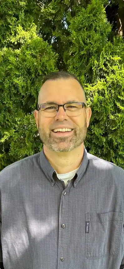 Merle Brovont, owner of Level Best Northwest, standing in front of a hedge